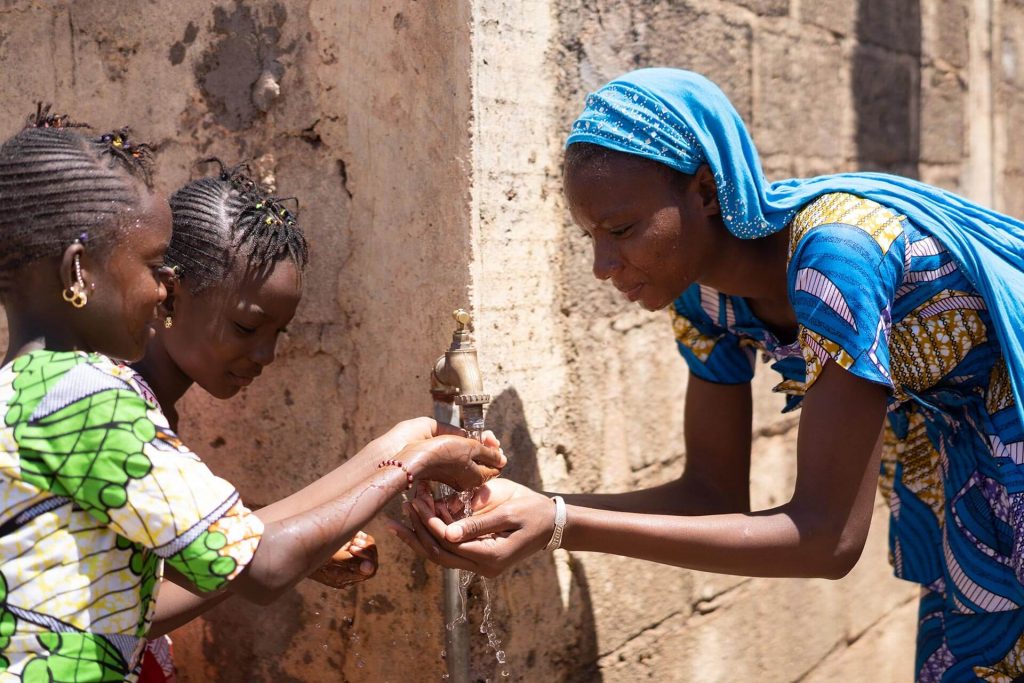 Woman and two girls sharing water from a tap